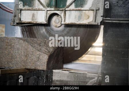 Elaborazione di granito in produzione. Il taglio di lastre di granito con una sega circolare. Utilizzo di acqua per il raffreddamento. Segatura industriale del granito Foto Stock