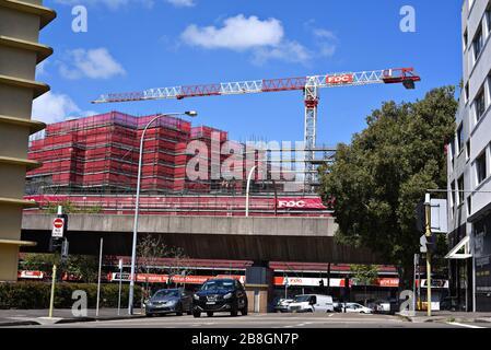 Un progetto di costruzione nella parte orientale di Sydney, una gru rossa e bianca che lavora su uno sviluppo residenziale sotto un accumulo di tessuto rosso da costruzione. Australia Foto Stock