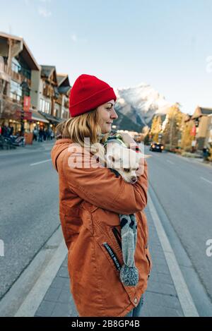 ragazza in una giacca arancione tiene una chihuahua tra le sue braccia vicino al lago, canada Foto Stock