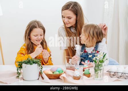 Madre amorevole che osserva le sue due figlie mentre dipingono le uova di pasqua dietro la tabella Foto Stock