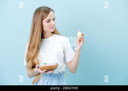 Felice donna compiaciuta in piedi con una ciotola di uova di pasqua in mani sopra blu Foto Stock