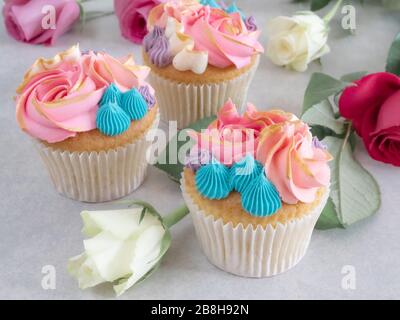 Tre cupcake con bella glassa tra alcune rose su un tavolo Foto Stock