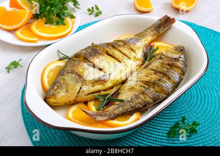 Pesce tostato con verdure e arance in una ciotola di ceramica. Menu dietetico Foto Stock