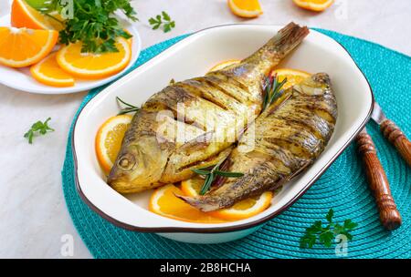 Pesce tostato con verdure e arance in una ciotola di ceramica. Menu dietetico Foto Stock