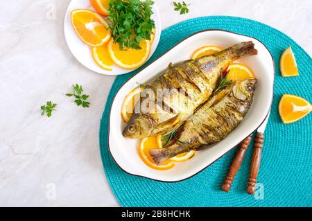 Pesce tostato con verdure e arance in una ciotola di ceramica. Vista dall'alto. Menu dietetico Foto Stock