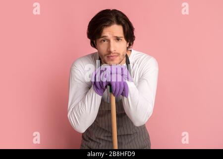 Uomo stanco che si appoggia all'impugnatura del mop, esaurito dopo la pulizia di primavera Foto Stock