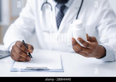 Medico generale africano che tiene le pillole scatola e scrittura Foto Stock