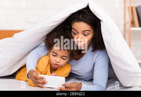 Mamma Africana e bambina che gioca Giochi Mobile a letto Foto Stock