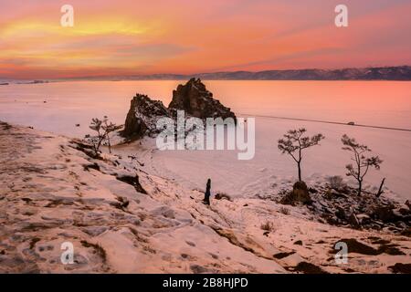Lago Baikal nel mese di dicembre. Magnifico paesaggio al tramonto dell'isola di Olkhon con il tempo nevoso. Vista del punto di riferimento naturale - Shamanka Rock e la Wish tre Foto Stock