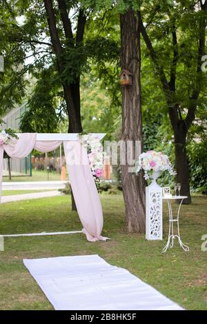 Arco di nozze, decorato da rose e sedie nel parco. Foto Stock