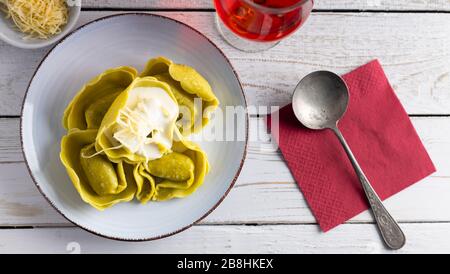 Tortellini biologici fatti in casa ripieni di spinaci e formaggio su un tavolo bianco con un bicchiere di vino a lato. Vista dall'alto. Foto Stock