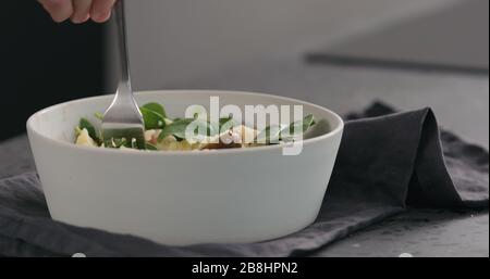 uomo mangia insalata con pomodori kumati e spinaci in ciotola bianca foto ampia Foto Stock