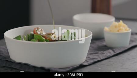 versare l'olio d'oliva nell'insalata con i pomodori kumati e gli spinaci in una ciotola bianca, foto ampia Foto Stock