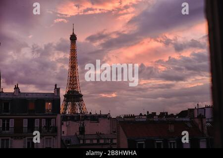 Torre Eiffel illuminata al tramonto con un crepuscolo rosa cielo nuvole viola e luci dorate, soffitta finestre e appartamenti rooflines in primo piano Foto Stock