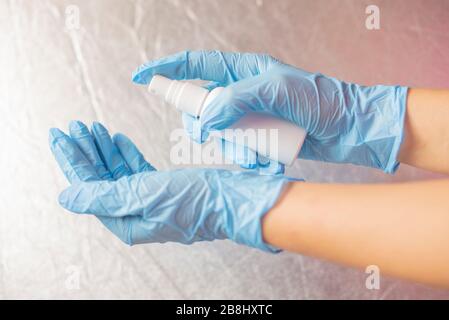 ragazza che tiene un antisettico contro i batteri in guanti di gomma blu su uno sfondo rosa Foto Stock