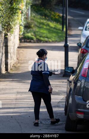 Cardiff, Galles, Regno Unito. 22 marzo 2020. CARDIFF, WALES, REGNO UNITO - 22 MARZO 2020 - un lavoratore del NHS che indossa una maschera facciale si avvicina a un'automobile dopo una visita domestica a Cardiff mentre il coronavirus accelera nel Regno Unito. Credit: Mark Hawkins/Alamy Live News Foto Stock