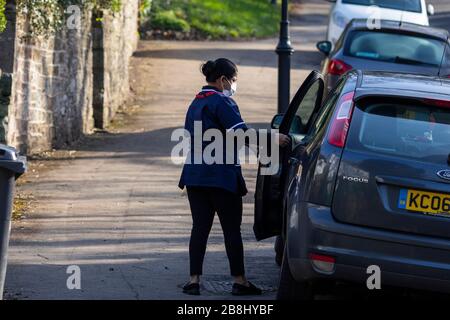 Cardiff, Galles, Regno Unito. 22 marzo 2020. CARDIFF, WALES, REGNO UNITO - 22 MARZO 2020 - un lavoratore del NHS che indossa una maschera facciale si avvicina a un'automobile dopo una visita domestica a Cardiff mentre il coronavirus accelera nel Regno Unito. Credit: Mark Hawkins/Alamy Live News Foto Stock