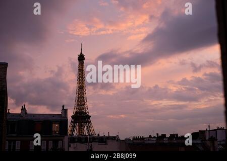 Torre Eiffel illuminata al tramonto di notte con nuvole blu cielo rosa e luci dorate, finestre soffitta e appartamenti tetto linee in primo piano Foto Stock