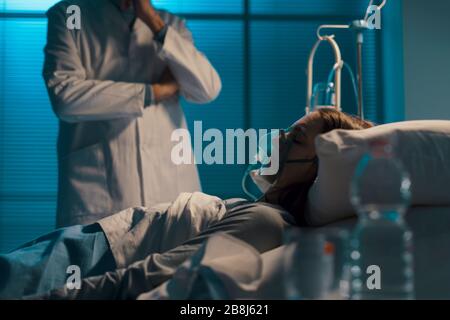 Medico professionista che controlla un paziente di notte, la donna è sdraiata a letto e dorme con una maschera di ossigeno Foto Stock