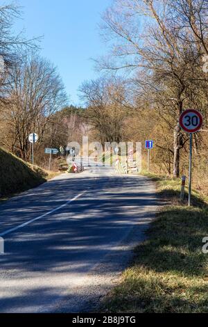 Riparazione di vecchia strada asfaltata nella campagna ceca. Limite di velocità. Strada in campagna. Strada dalle ombre. Mattina di primavera su strada di campagna. Foto Stock