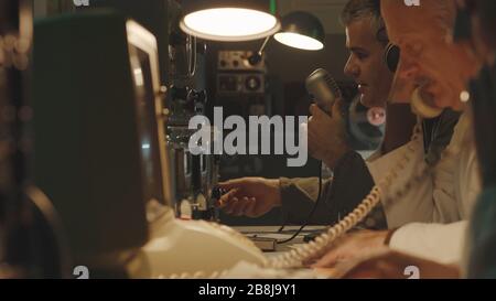 Team di scienziati che lavorano in una sala di controllo in stile vintage, utilizzano computer e fanno telefonate Foto Stock