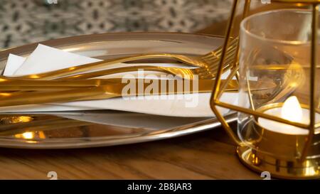 Posate d'oro su un vassoio d'argento pronte per servire del cibo a colazione, pranzo o cena accanto ad una lampada dorata Foto Stock