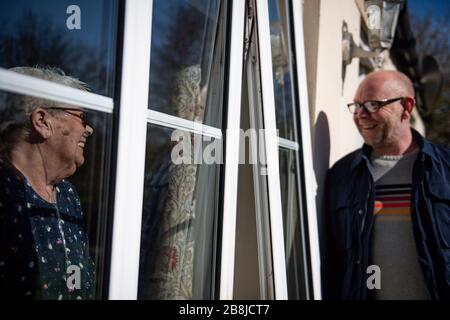 Olive Trotman, 76 anni, è visitata nel giorno della Madre da suo figlio Mark Trotman. L'oliva soffre di malattia polmonare ostruttiva cronica (BPCO) ed enfisema, e sta prendendo la precauzione di comunicare ad una distanza di sicurezza o attraverso una finestra di vetro, per limitare la diffusione potenziale di coronavirus. Data foto domenica 22 marzo 2020. Vedi la storia PA SALUTE Coronavirus. Il credito della foto dovrebbe leggere: Jacob King/PA Wire Foto Stock