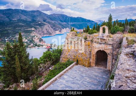 Vecchio cancello forte sulla cima della penisola di frourio e villaggio di Assos con bella baia di mare e cipressi sullo sfondo. Isola di Cefalonia, Grecia Foto Stock