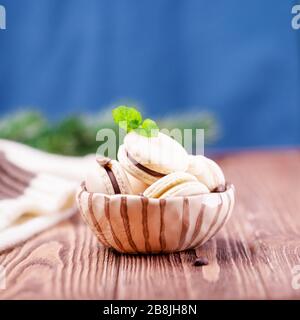 Macaroni di cioccolato alla vaniglia o macaron francesi fatti in casa con foglia di menta su uno sfondo classico di colore blu Foto Stock