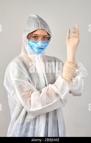 Ragazza che indossa un'uniforme protettiva antivirale indossando guanti di gomma. Foto Stock