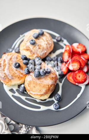 Pancake o sciroppi di formaggio casolare con mirtillo e fragole su piatto nero, vista primo piano. Salsa di latte condensato. Cucina russa, Ucraina Foto Stock