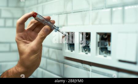 Stretta di mano maschio tenendo un cacciavite, controllo presa nuova casella nell'appartamento. Inquadratura orizzontale. Vista laterale Foto Stock