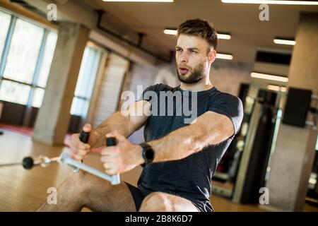 Bel giovane uomo che usa una macchina da file seduta in palestra Foto Stock