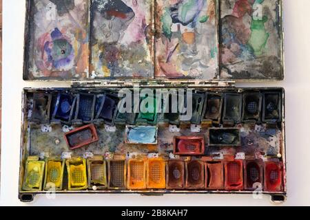 Vecchie vernici acquerello in una vista dall'alto del contenitore di plastica. Sporco insieme di vernice acquerello di colori diversi in fossati. Confezionamento di vernice acquerello asciutta Foto Stock