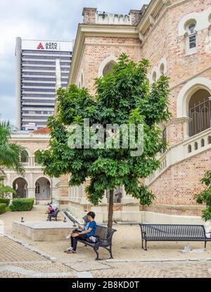 Coppia seduta su una panchina di metallo lungo il passaggio pedonale River of Life al Sultan Abdul Samad Building Kuala Lumpur Malesia. Foto Stock