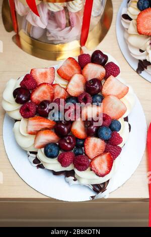 Torta Pavlova con fragole fresche, ciliegie, mirtilli e lamponi, cioccolato fuso e panna montata. Foto Stock