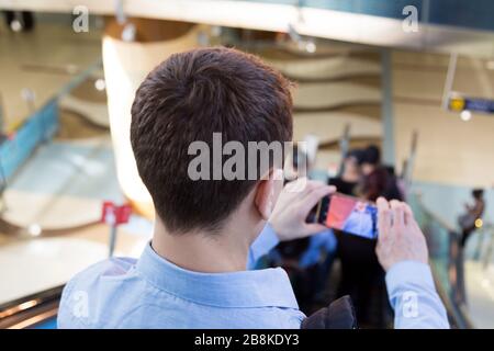 Un uomo toglie i passeggeri della metropolitana sul suo smartphone scendendo dalla scala mobile. Foto Stock