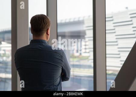 Un uomo di 40-45-anno in una camicia blu a quadri si pone nel corridoio posteriore dell'ufficio in mezzo ad una grande finestra. Foto Stock