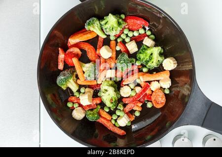 Friggere le verdure surgelate in una padella. Primo piano della vista dall'alto prefabbricata. Foto Stock