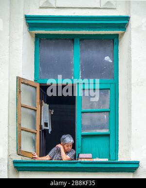 Donna anziana seduta alla finestra del suo appartamento che guarda la strada sottostante, Jalan Tuanku Abdul Rahman Kuala Lumpur Malesia. Foto Stock