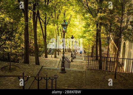 La mattina presto a Montmartre Steps, Parigi, Francia in una mattina soleggiata e calda in autunno, come la luce del sole splende attraverso il baldacchino delle foglie Foto Stock