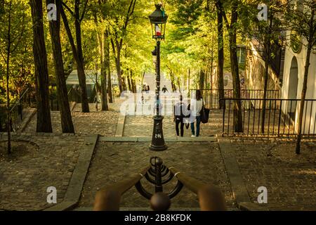 Gli studenti camminano lungo la scalinata di Montmartre alla luce del sole di prima mattina, Parigi, Francia, mentre la luce del sole splende attraverso il baldacchino delle foglie Foto Stock