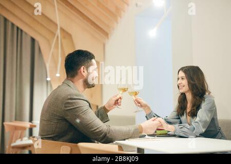 Ritratto con vista laterale di coppia moderna con bicchieri da champagne mentre ti godi la data in un caffè, spazio per fotocopie Foto Stock