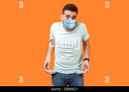 Ritratto di frustrato uomo preoccupato con maschera medica in casual bianco t-shirt che risulta tasche vuote che mi mostrano non ho denaro gesto, in fallimento. indo Foto Stock