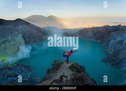 Yoga posare in una posizione più esotica rispetto a una palestra o uno studio. Una persona coraggiosa che fa una posa di yoga al Cratere di Ijen, Indonesia. Foto Stock