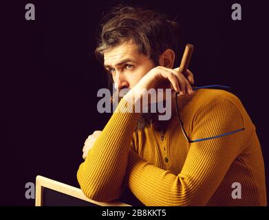 bell'uomo a pelo con lunghi baffi lussureggianti della barba e capelli eleganti sul viso premuroso in occhiali e maglione giallo che tiene, sigaro da fumo bordo in studio su sfondo nero Foto Stock