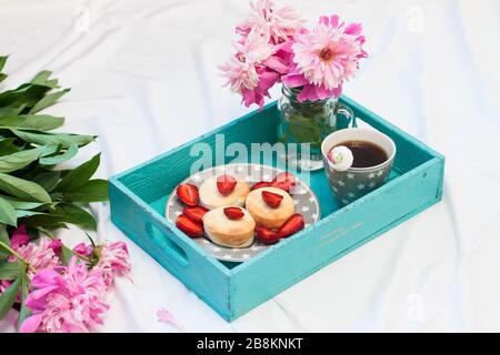 Colazione a letto con frittelle di formaggio casolare, fragole fresche, peonie e una tazza di caffè. Sfondo bianco. Foto Stock