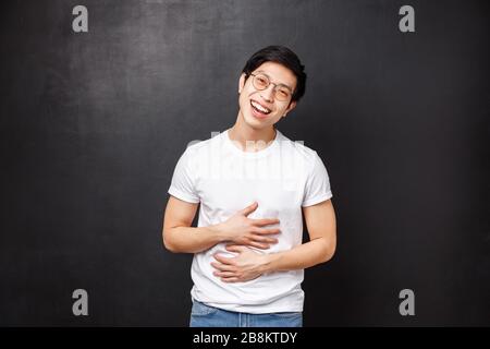 Ritratto del carismatico ragazzo asiatico amichevole in occhiali e t-shirt, appendere-out con gli amici, divertirsi, inclinare la testa sorridendo e ridendo, riempire il dolore in Foto Stock