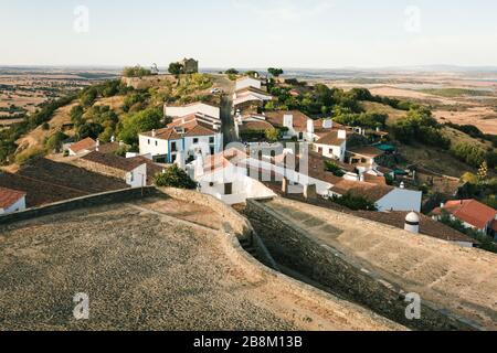 Monsaraz villaggio, vicino alla diga di Alqueva, in Portogallo, al tramonto, con le case tipiche di Alentejo in primo piano e i campi di grano sullo sfondo Foto Stock