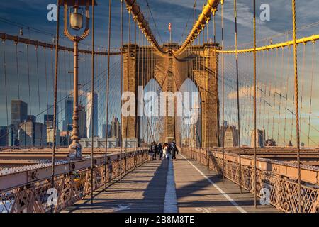 Ponte di Brooklyn con vista diurna a New York con persone che camminano, la bandiera americana in cima e i lucernari sullo sfondo Foto Stock